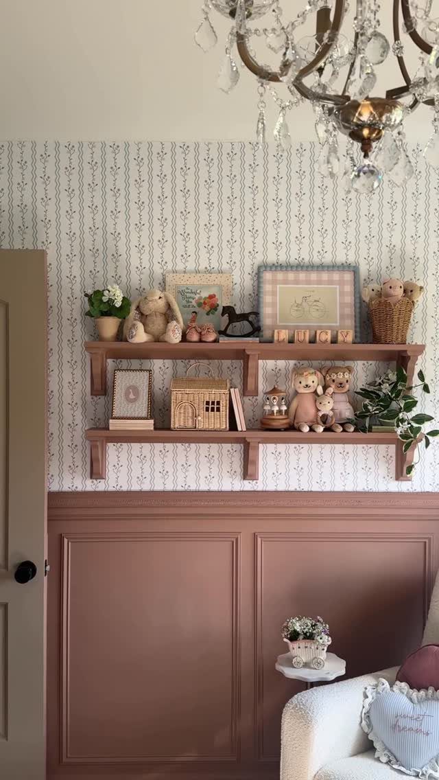Dusty rose half-height wainscoting paired with patterned wallpaper and wooden floating shelves holding small toys.