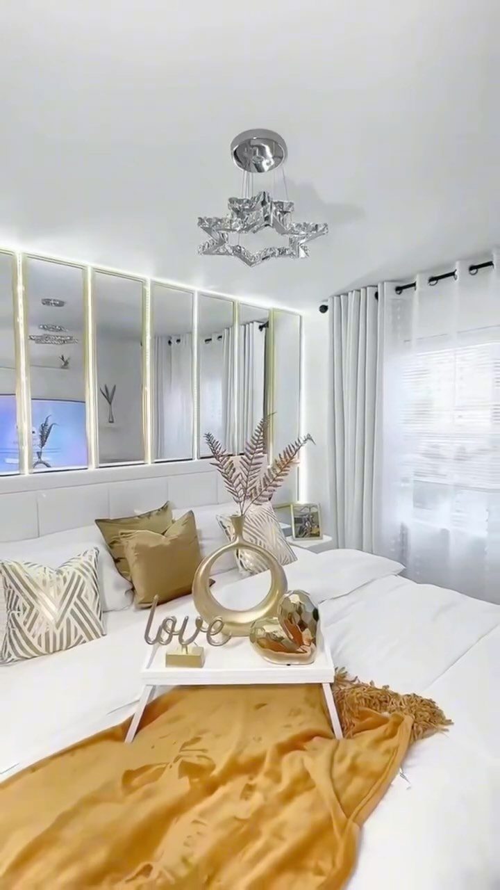 Large vertical mirrors mounted on a bedroom wall behind a white bed with gold accents.