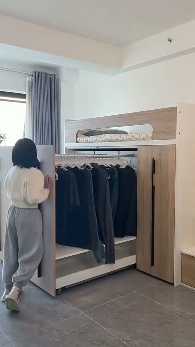 A person stands beside a light wood loft bed unit with a built-in clothing rack underneath.