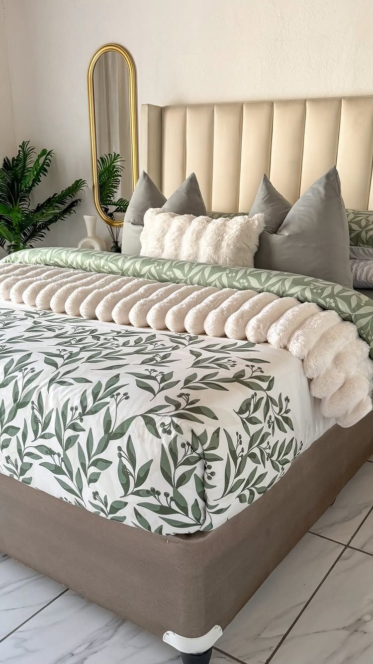 A bed decorated with leaf-patterned linens, grey pillows, and a white textured faux-fur throw blanket.