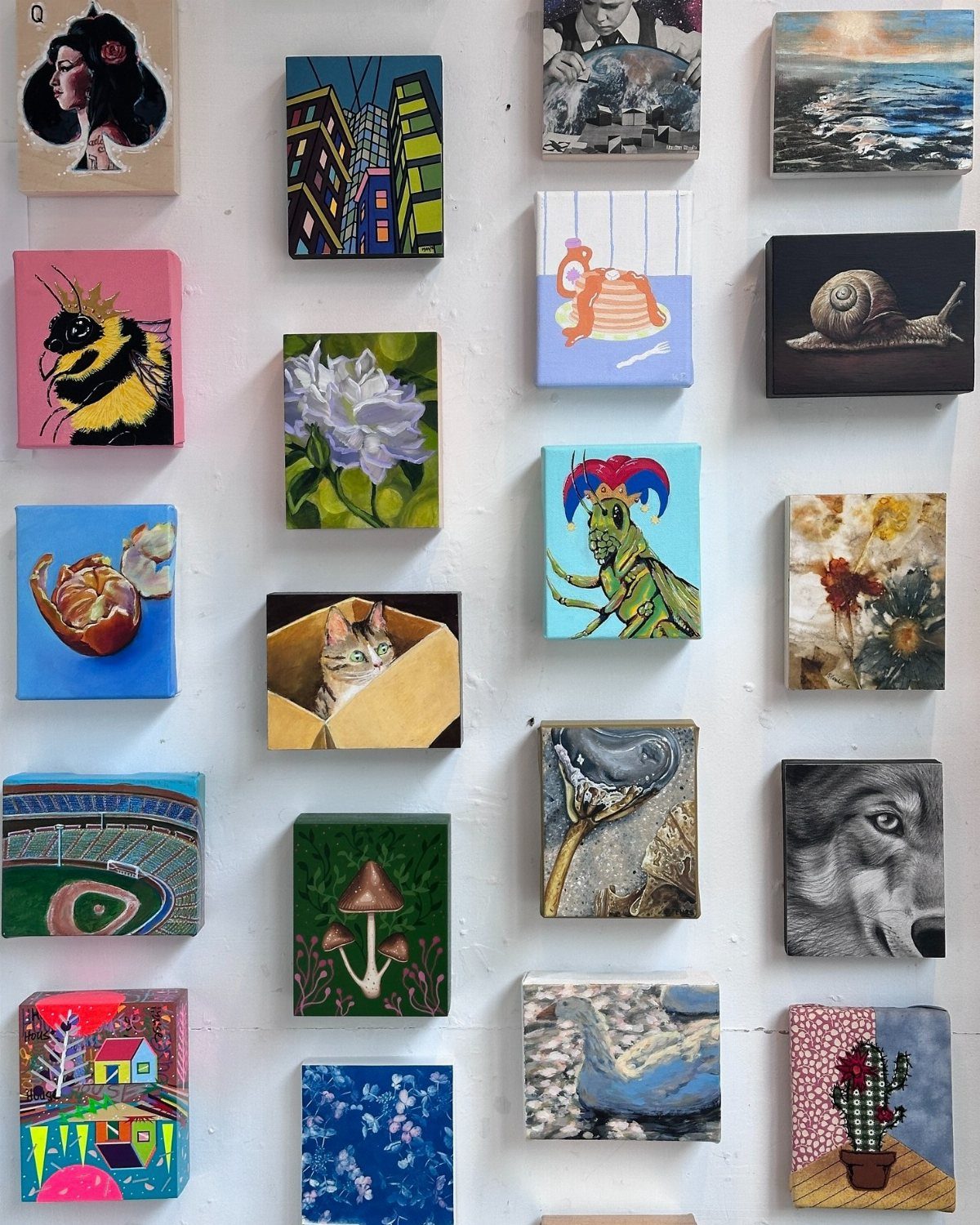 Small colorful paintings and sketches arranged in a gallery style on a white wall.
