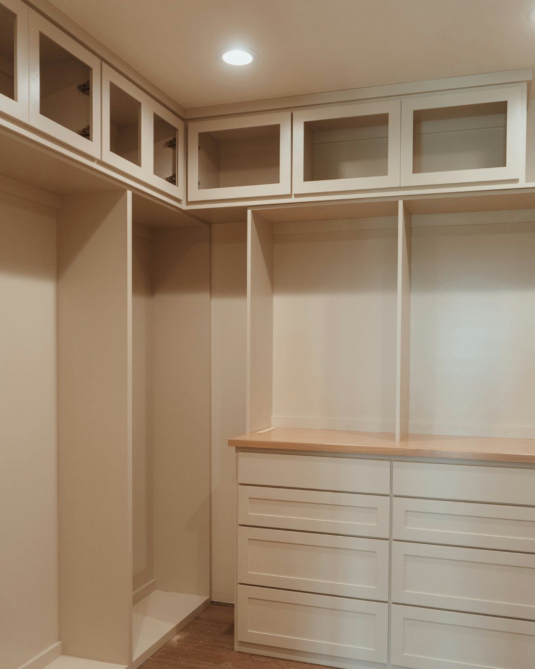 Cream colored built-in closet system with glass upper cabinets and wooden countertop drawers.