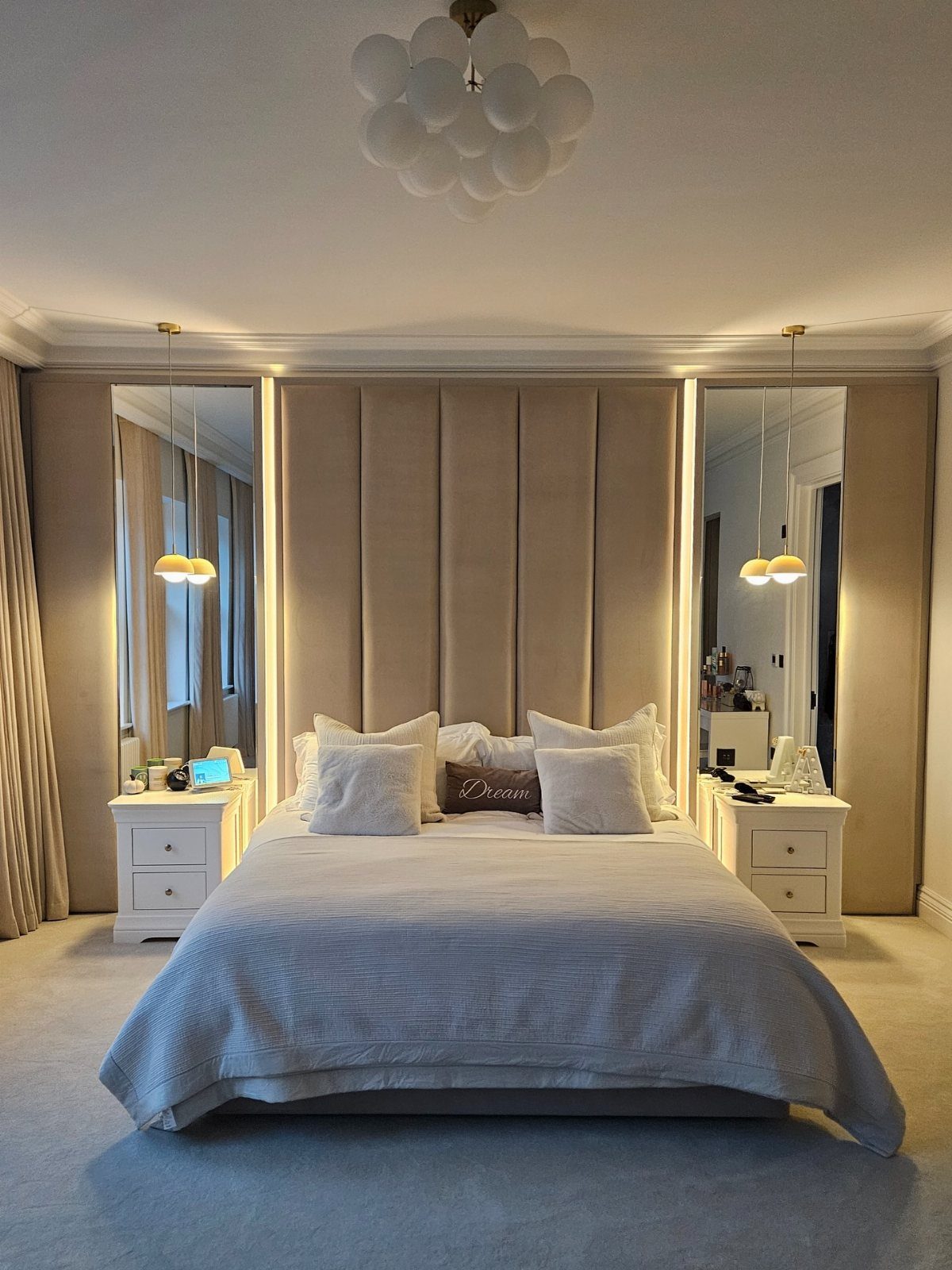 A large bed with a tall beige upholstered wall panel headboard and mirrors.