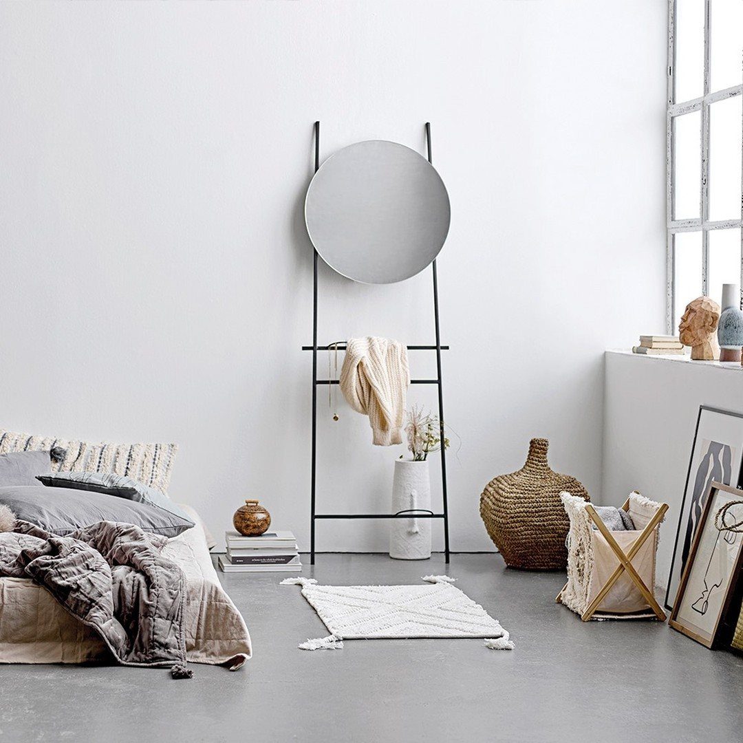 Minimalist bedroom featuring a low bed, a large round mirror on a black stand, and woven decor.