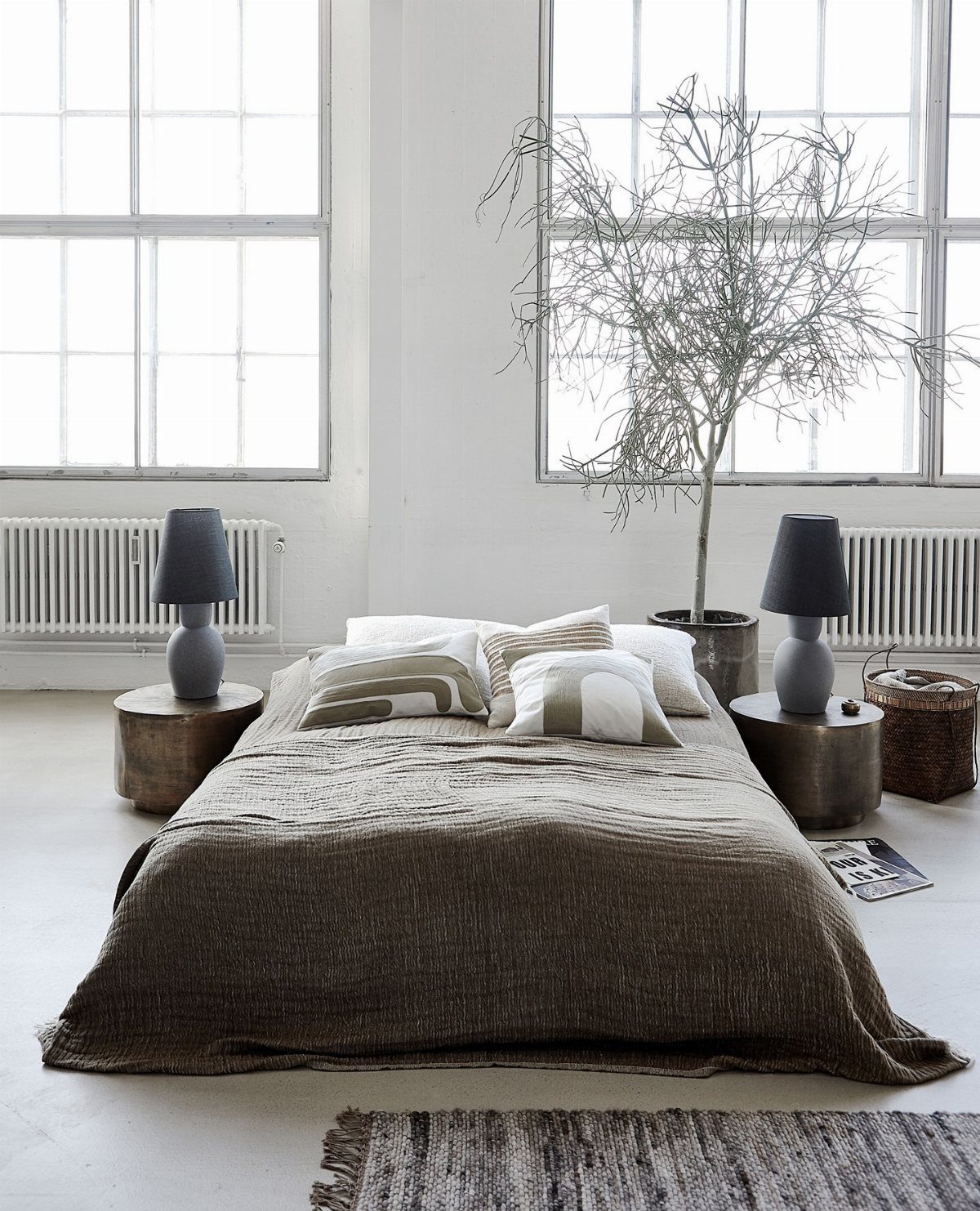 Low bed with textured brown bedding and patterned pillows in a bright, minimalist room.