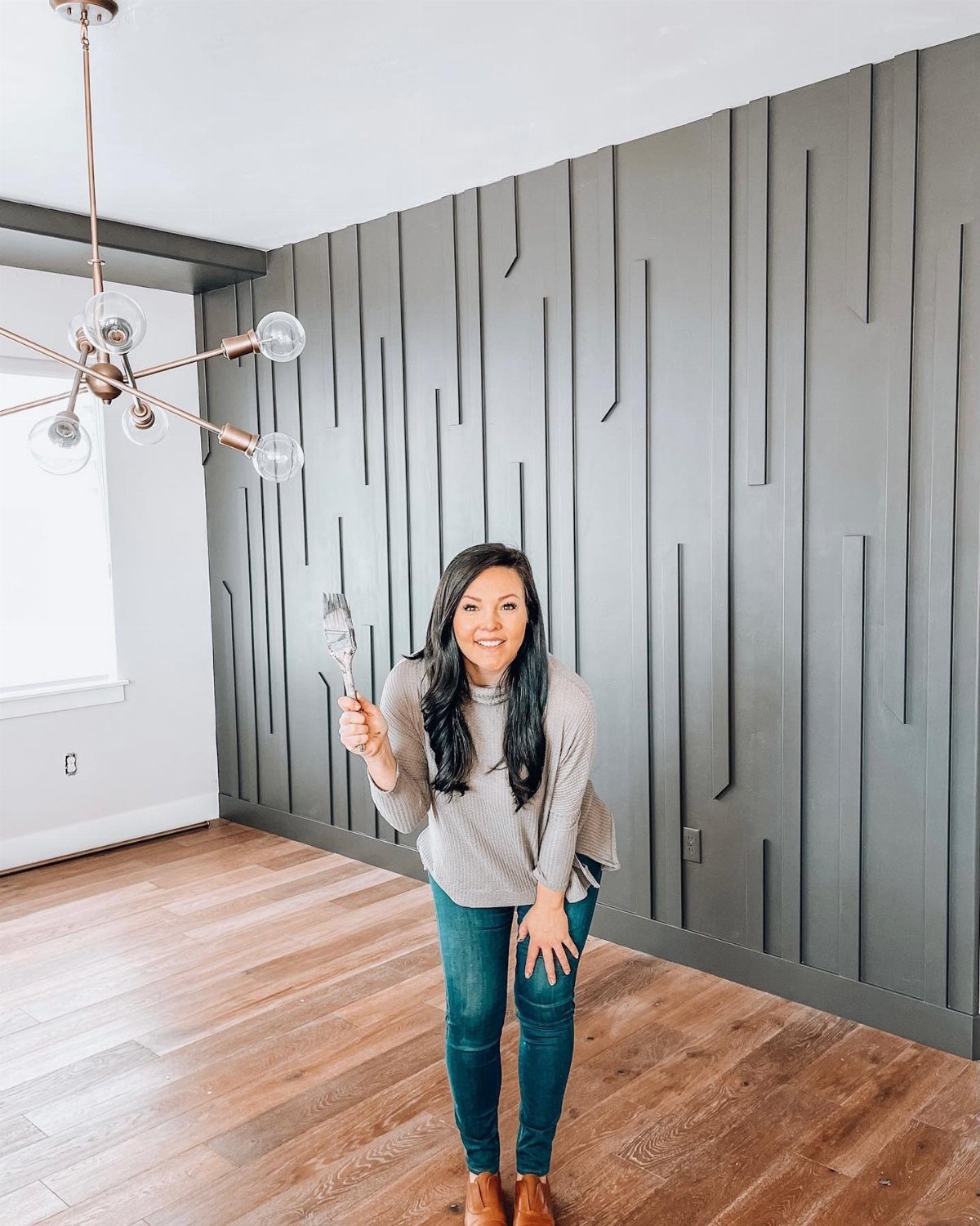 Woman holding a paintbrush in front of a gray vertical slat accent wall.