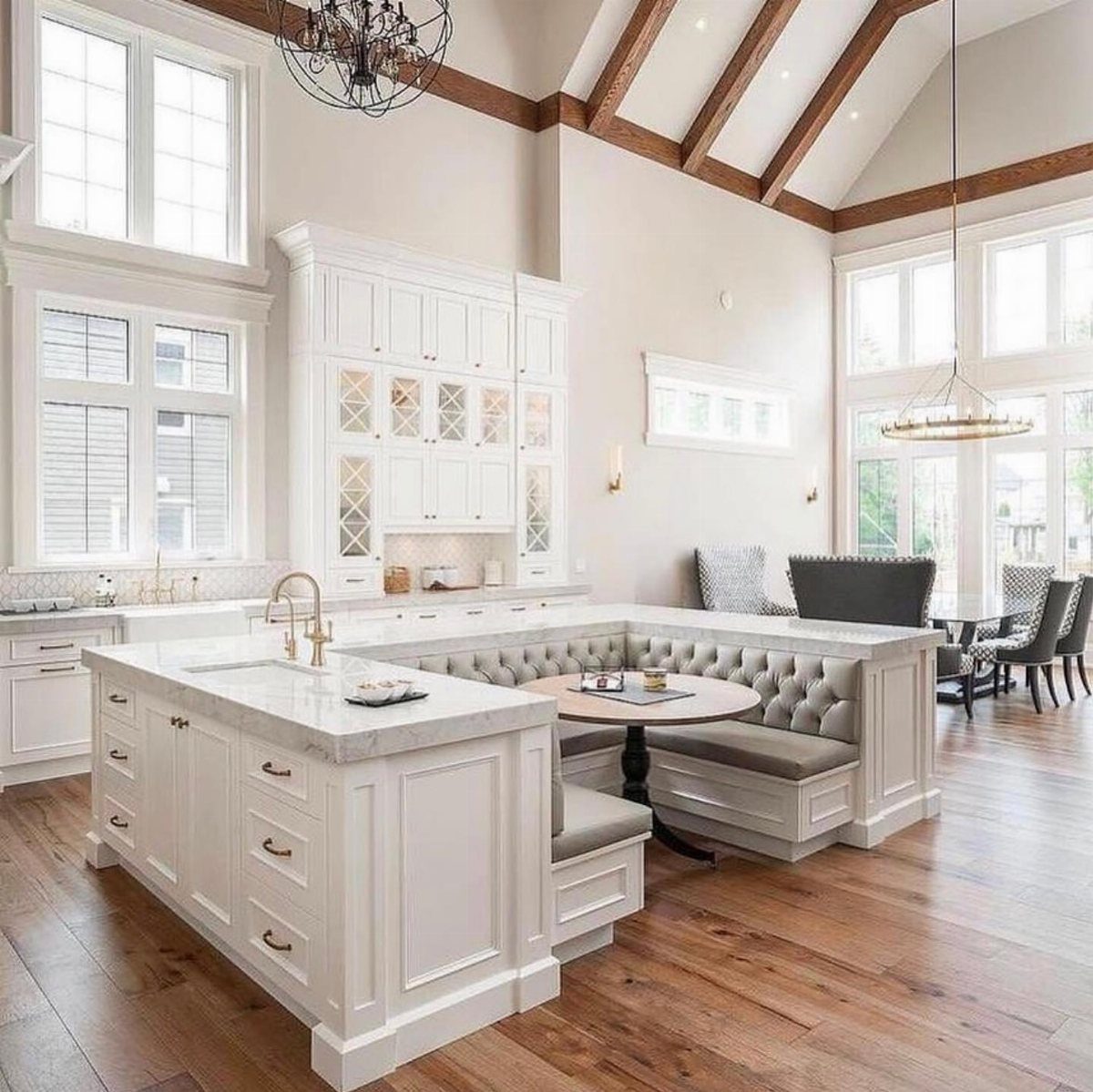 White kitchen island with a built-in grey tufted banquette seating around a round table.