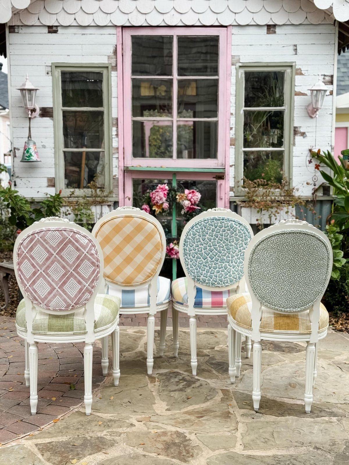 Four white wooden chairs with various colorful patterned fabric upholstery on a stone patio.