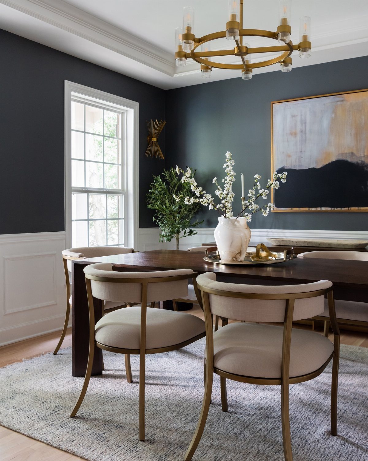 Dark grey dining room with a wooden table, gold chairs, and a brass chandelier.