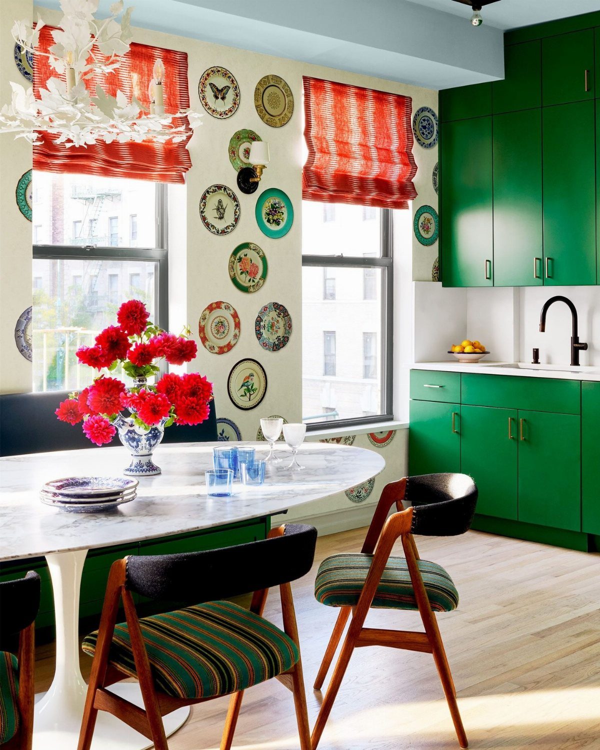 A marble dining table with red flowers and patterned plates on the walls in a small room.