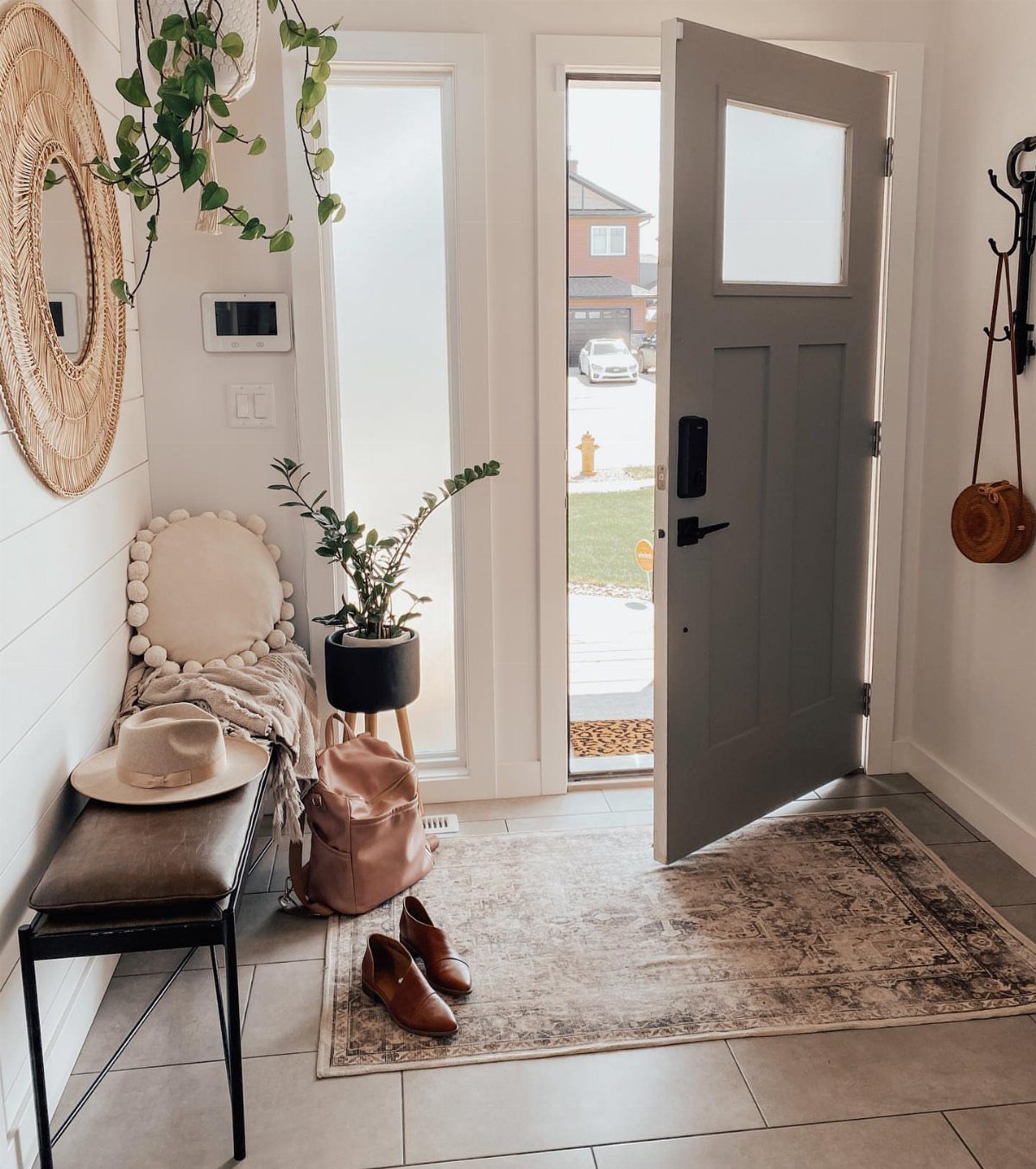 Patterned rug on a tiled entryway floor next to an open grey door and a small bench.
