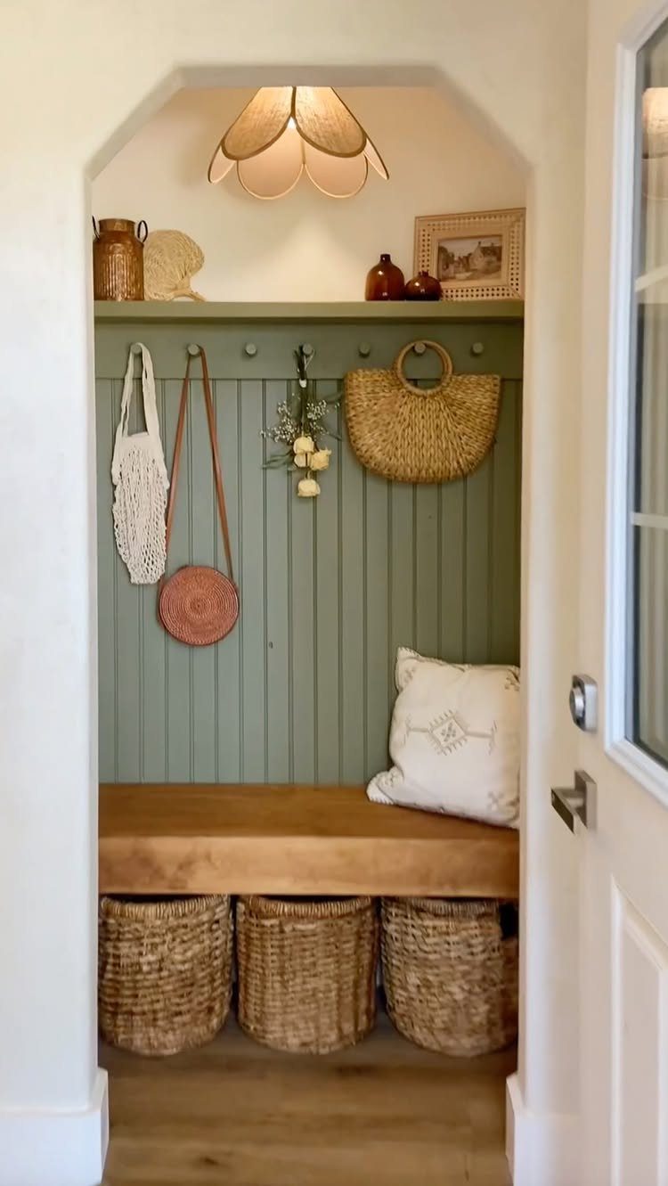Built-in mudroom nook with a wooden bench, sage green beadboard, and woven storage baskets.