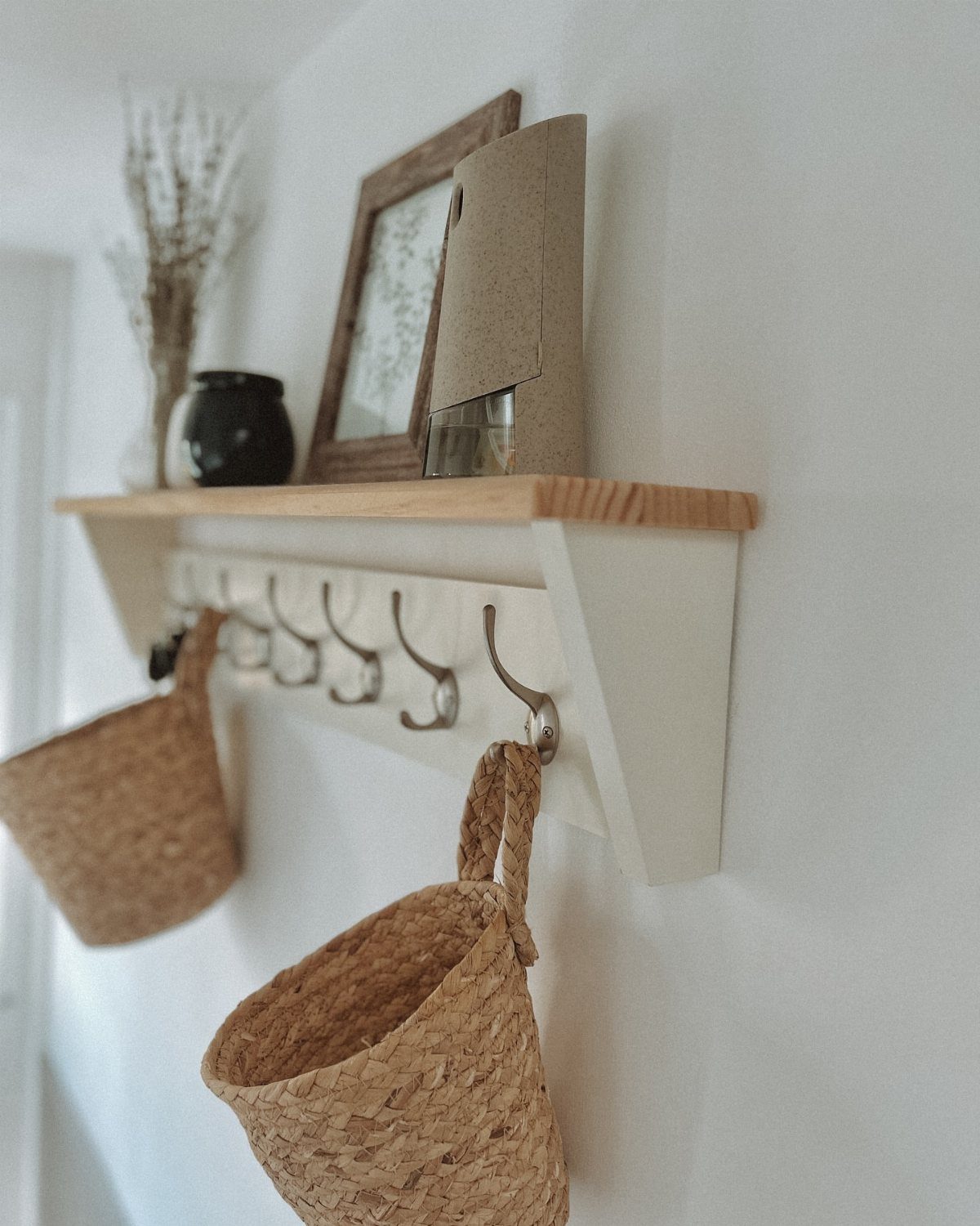 Two woven seagrass baskets hanging from metal hooks on a white wall shelf.
