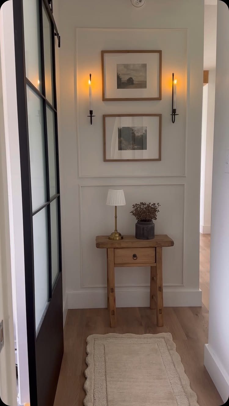 Black wall sconces illuminating framed art above a wooden console table in an entryway.