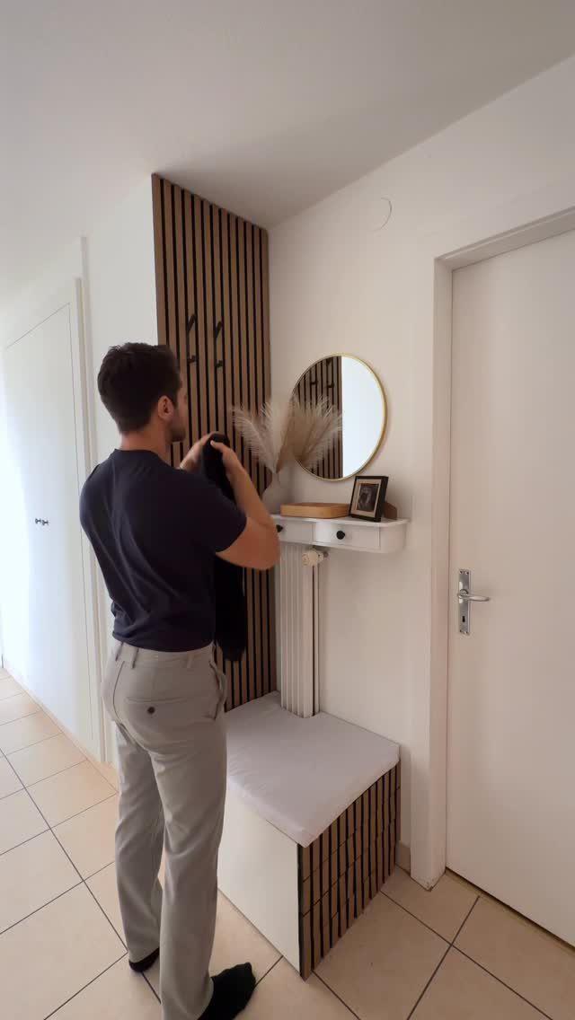 Man standing in a bright entryway featuring a wood slat wall and white storage bench.