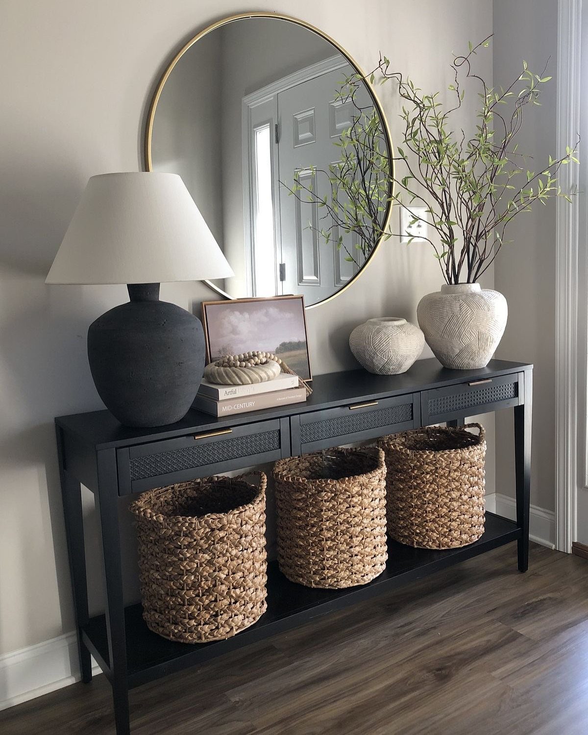 Three woven wicker baskets stored on the bottom shelf of a black console table.
