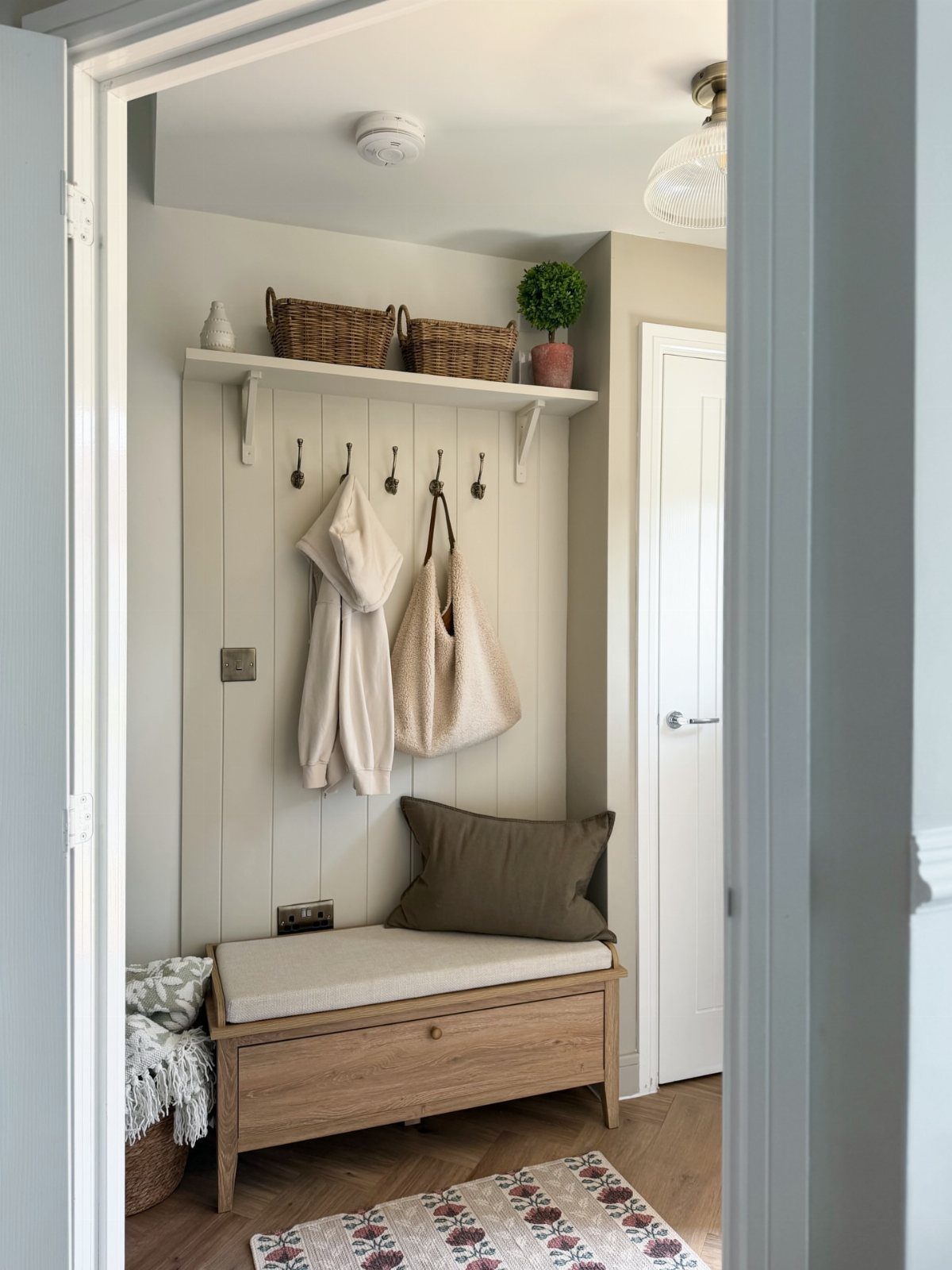 Wooden storage bench with a cushion sits in a small entryway with wall hooks.