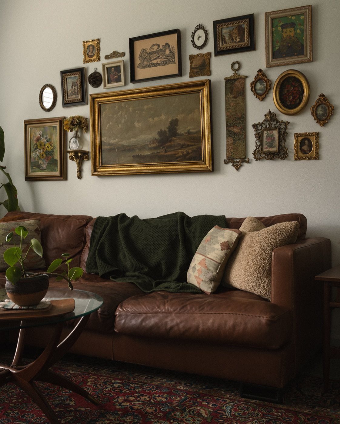 A collection of framed art pieces arranged in a gallery wall above a brown leather sofa.