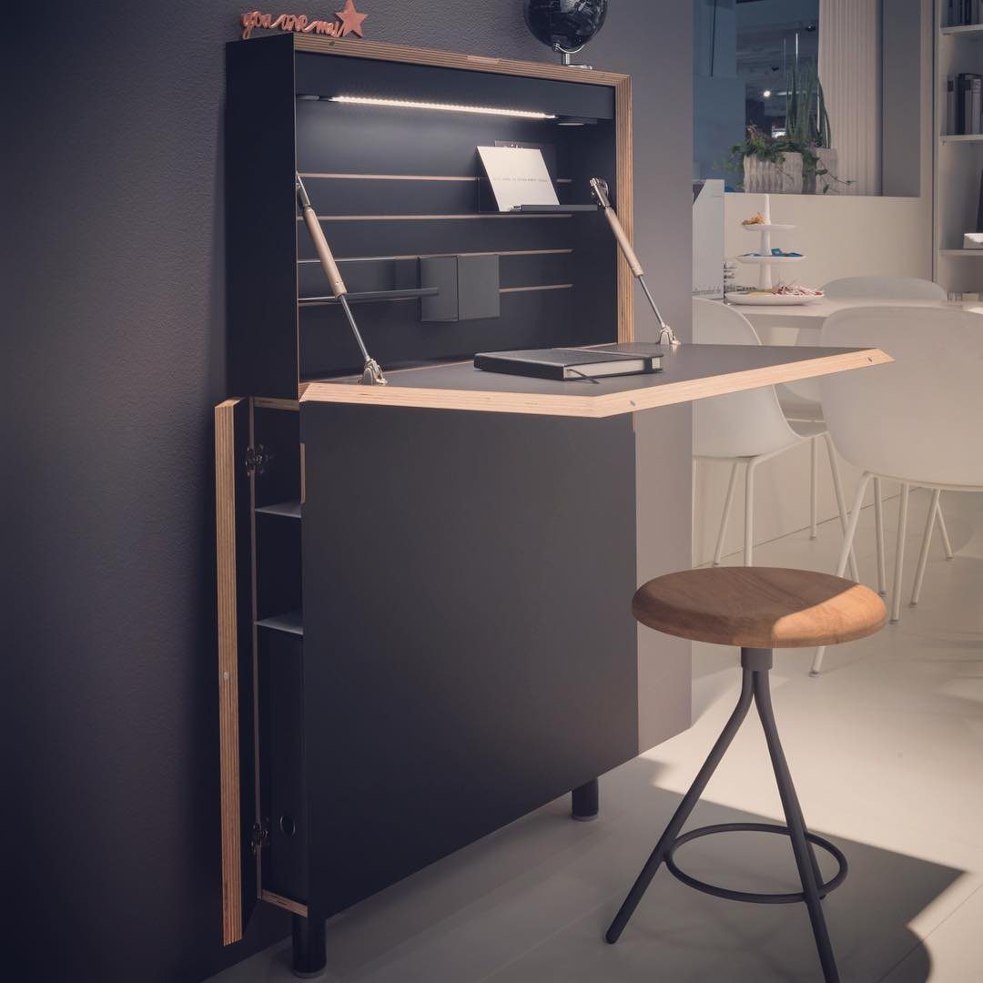 A dark grey wall-mounted secretary desk with light wood trim and a wooden stool.