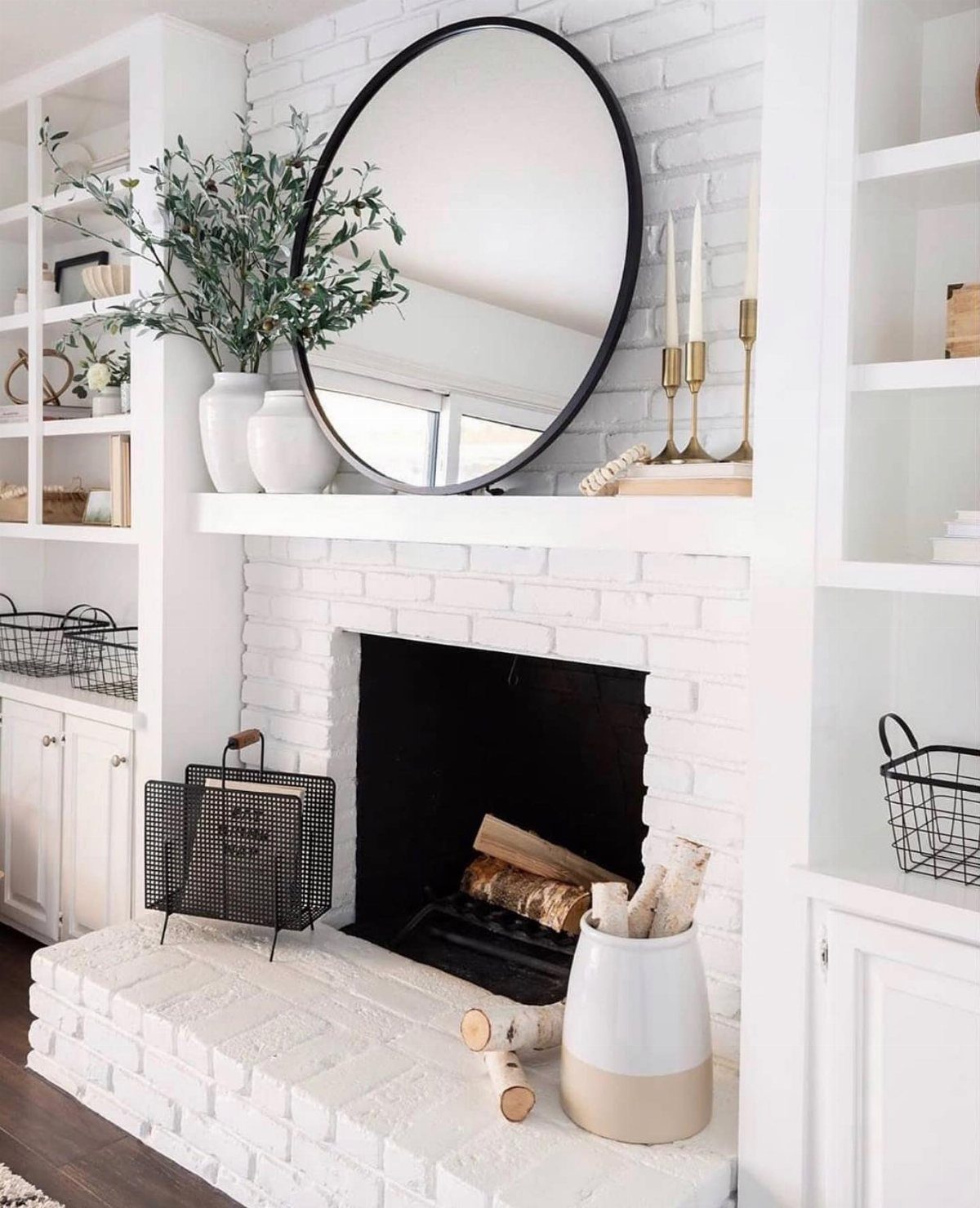A white brick fireplace with a large round mirror and greenery on the mantel.