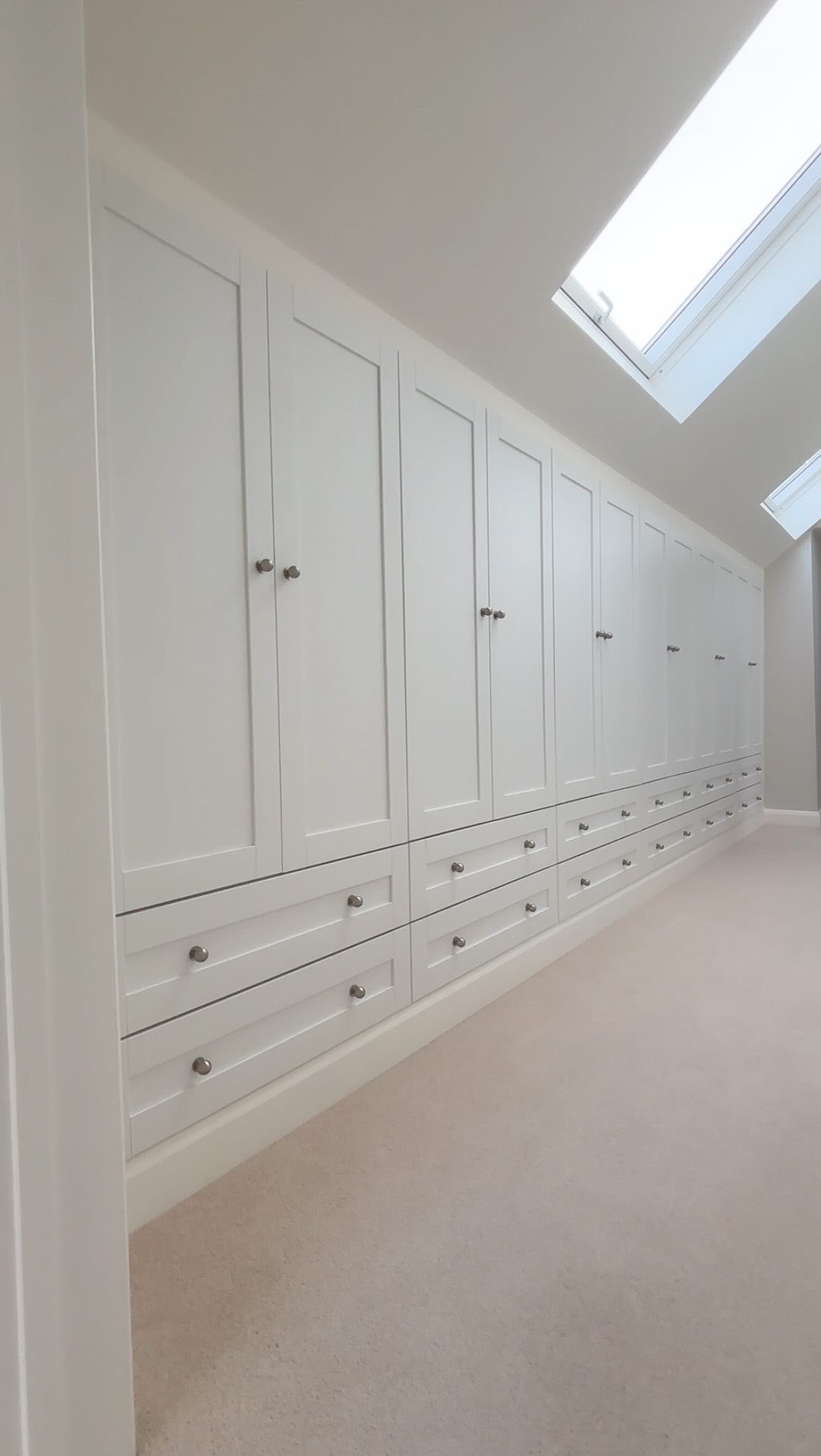 Built-in white storage cabinets with silver knobs and drawers along a light-colored wall.