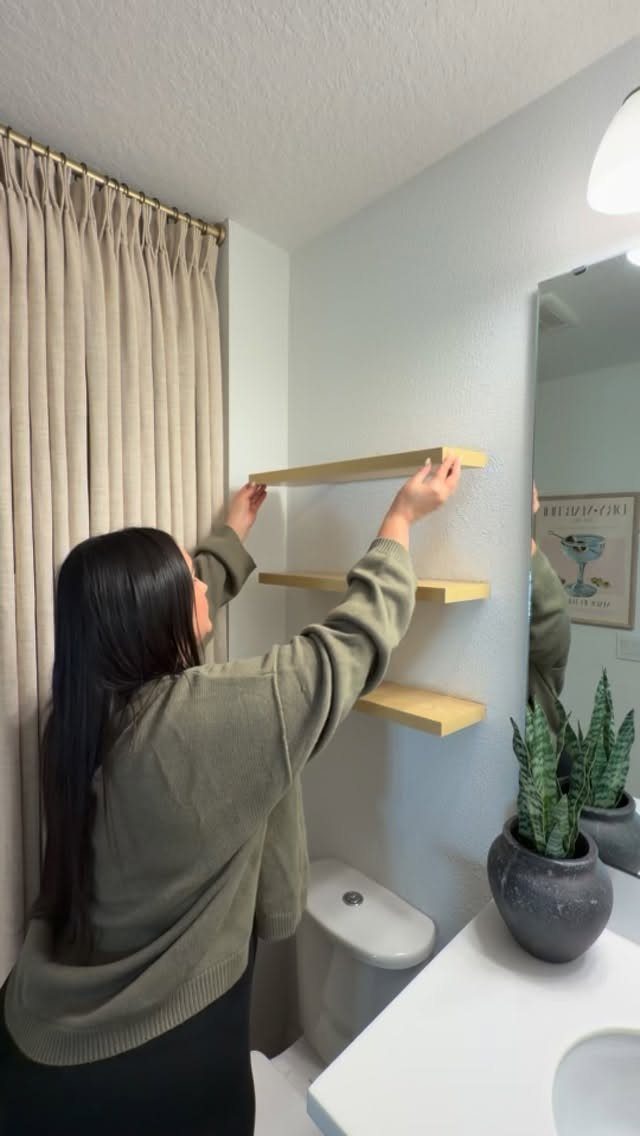 A person installing three wooden floating shelves onto a light blue wall in a room.