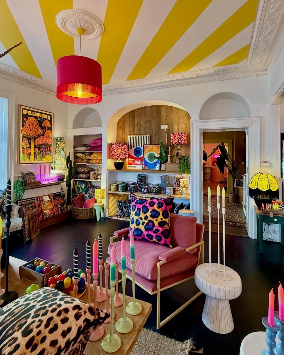 Maximalist living room with striped ceiling, pink velvet chair, leopard print pillows, and colorful candles.