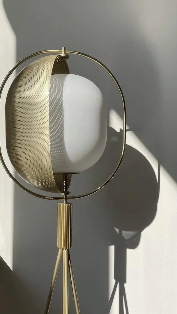 A modern gold tripod floor lamp with a white spherical diffuser against a white wall.