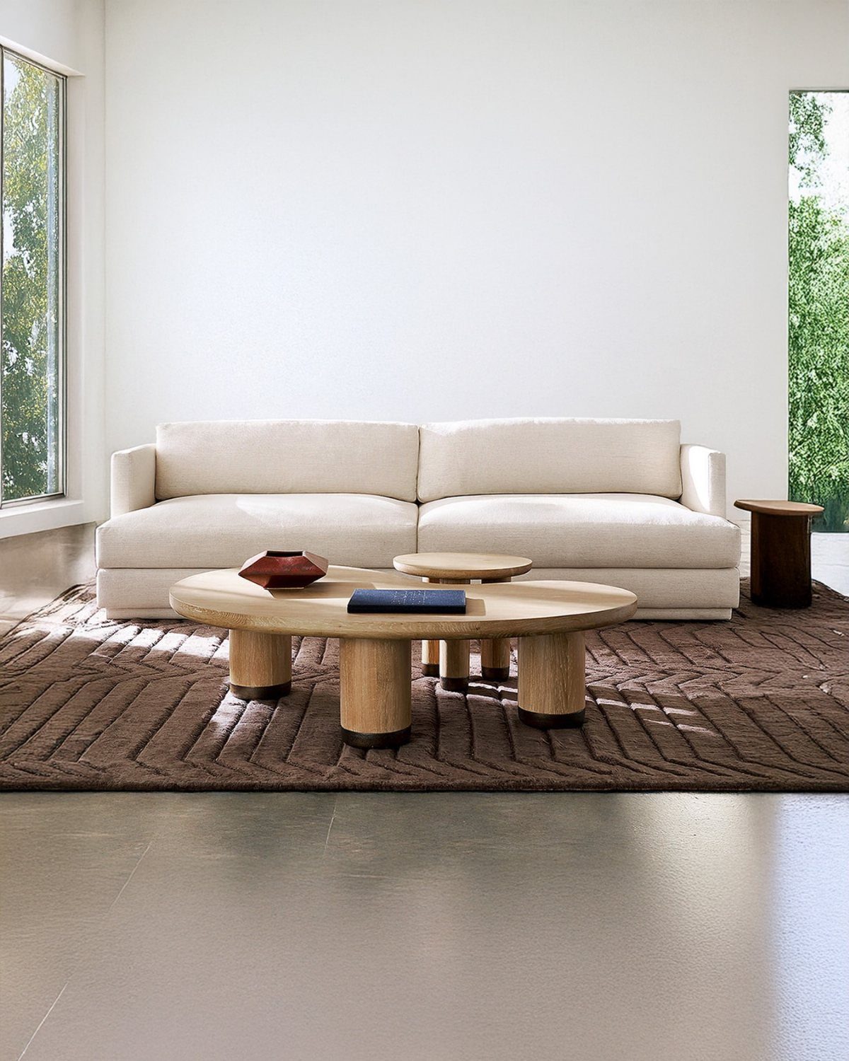 A cream low-profile sofa sits on a brown textured rug with wooden coffee tables.