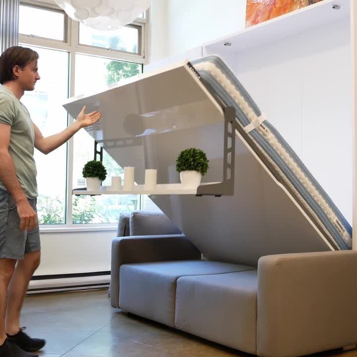 A man demonstrates a white wall-mounted piece of multi-functional furniture with small plants.
