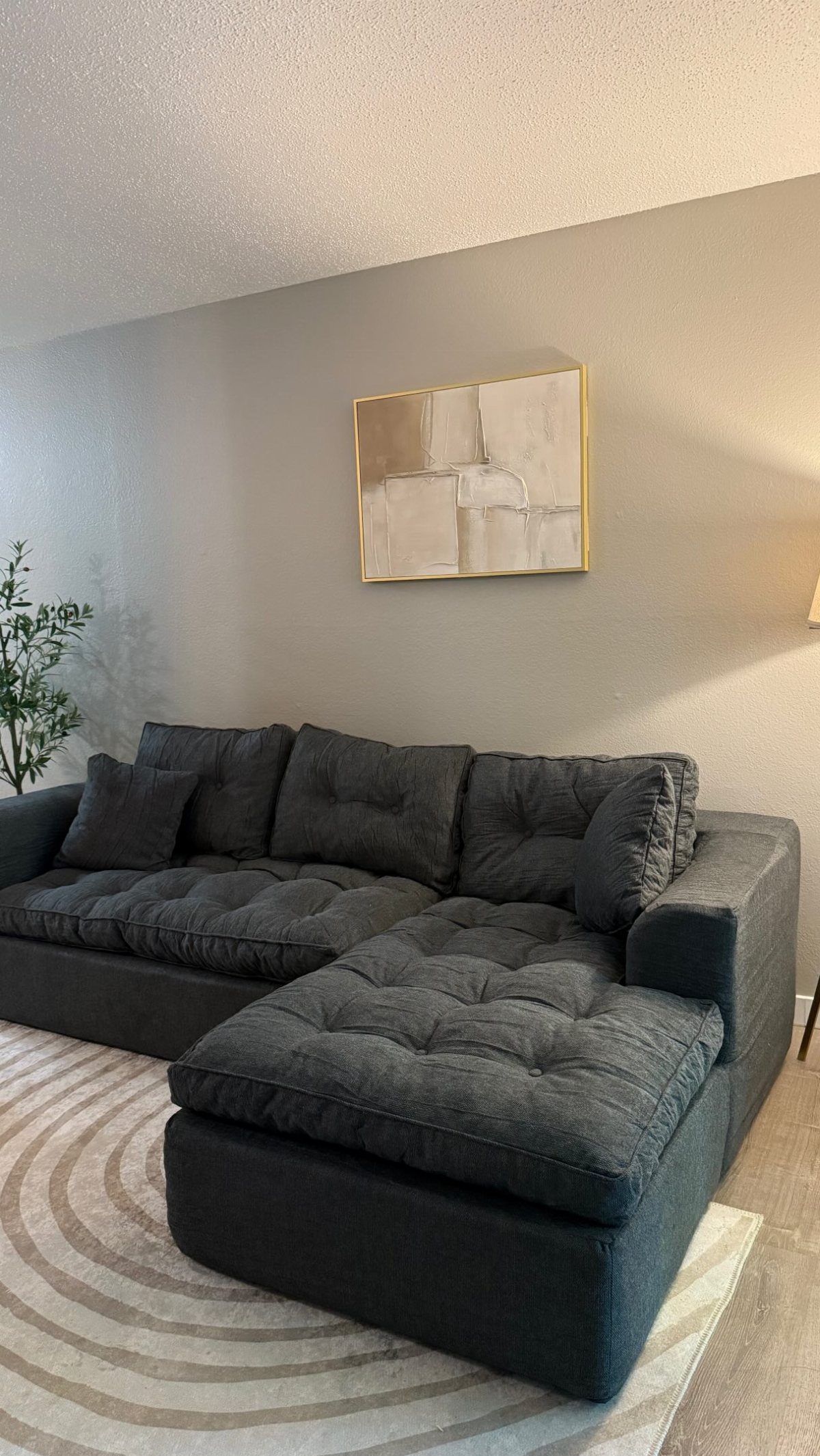 A dark grey fabric sectional sofa positioned on a striped rug against a grey wall.
