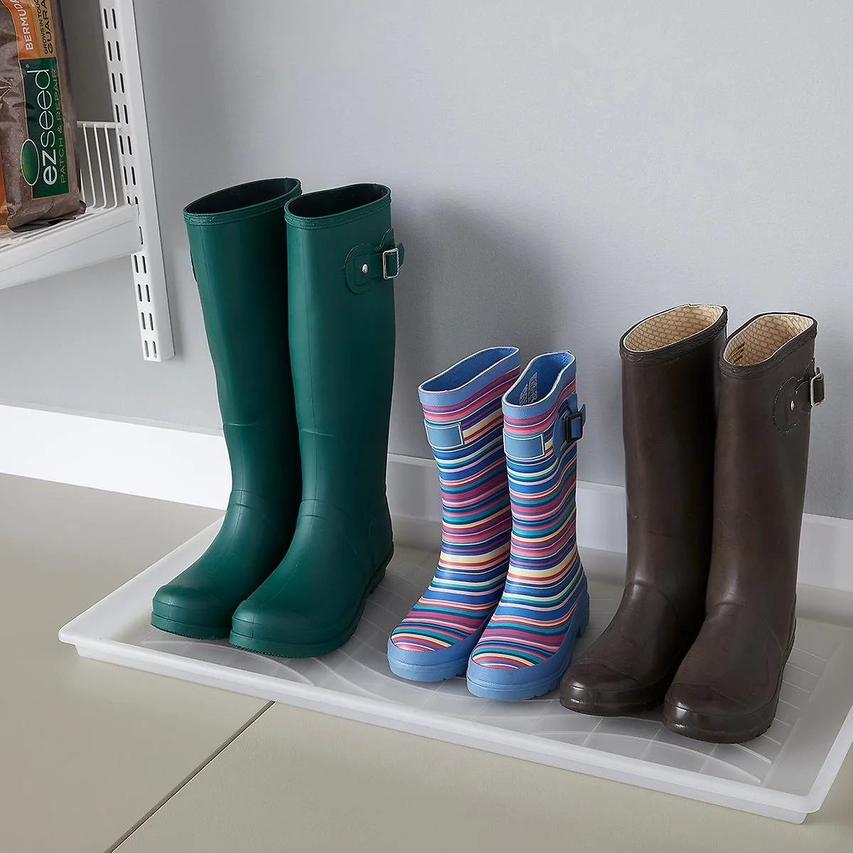 Three pairs of colorful rubber rain boots resting inside a white plastic boot tray.
