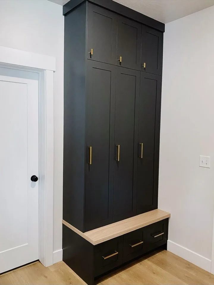 Tall dark built-in cabinetry with gold hardware and a light wood bench against a white wall.