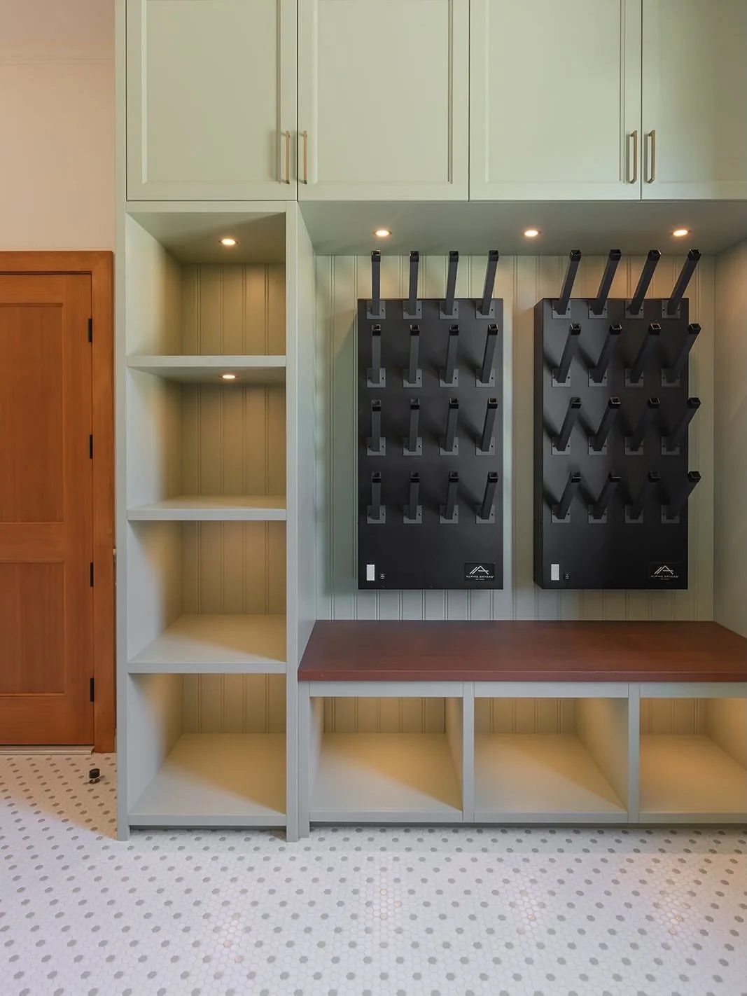 Custom sage green cabinetry with built-in shelving, a wooden bench, and black wall-mounted hooks.