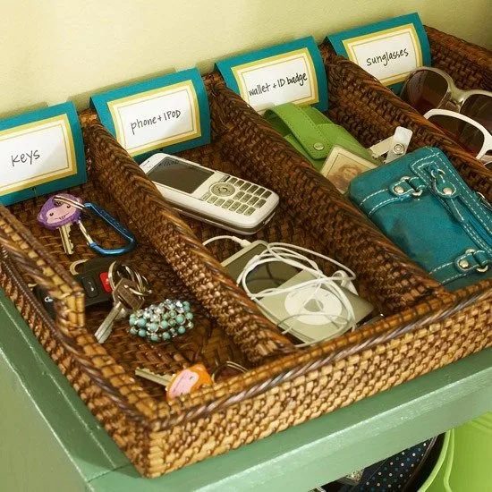 Woven wicker trays holding keys, a phone, a wallet, and sunglasses on a green shelf.