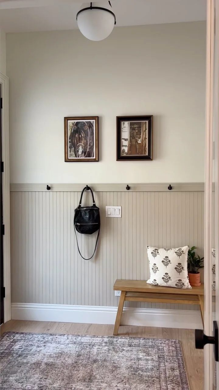 Black wall hooks on beadboard wainscoting holding a black handbag above a wooden bench.