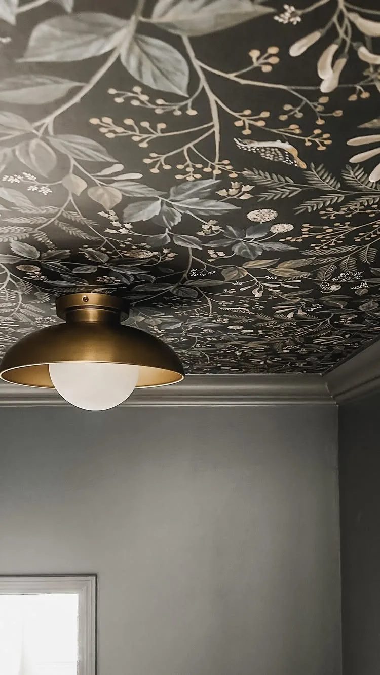 Brass dome ceiling light with a white globe against a dark botanical patterned ceiling.