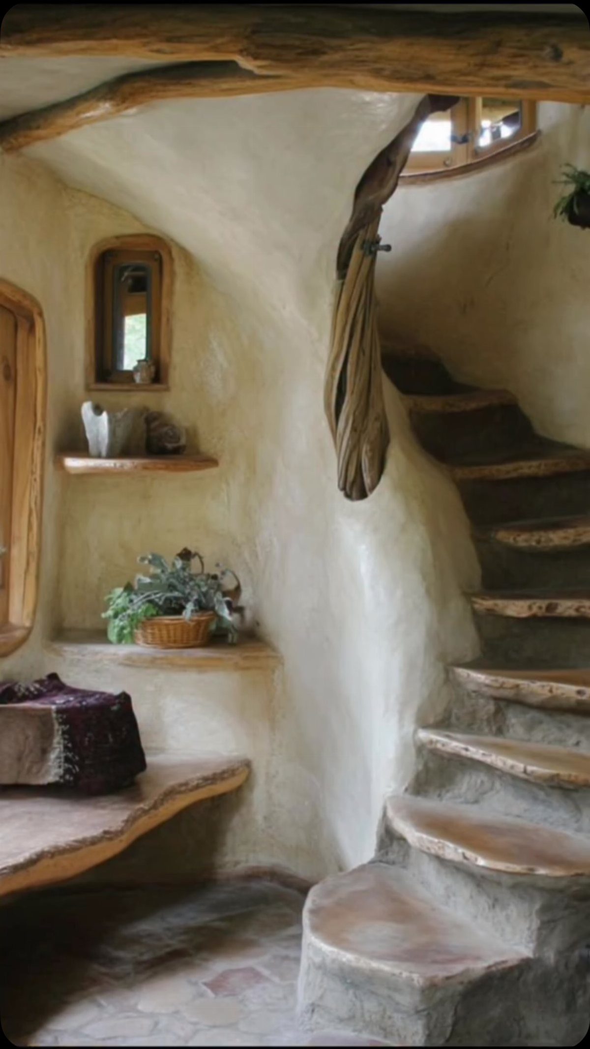 Curved plaster walls and stone stairs with natural wood slab treads in a rustic room.