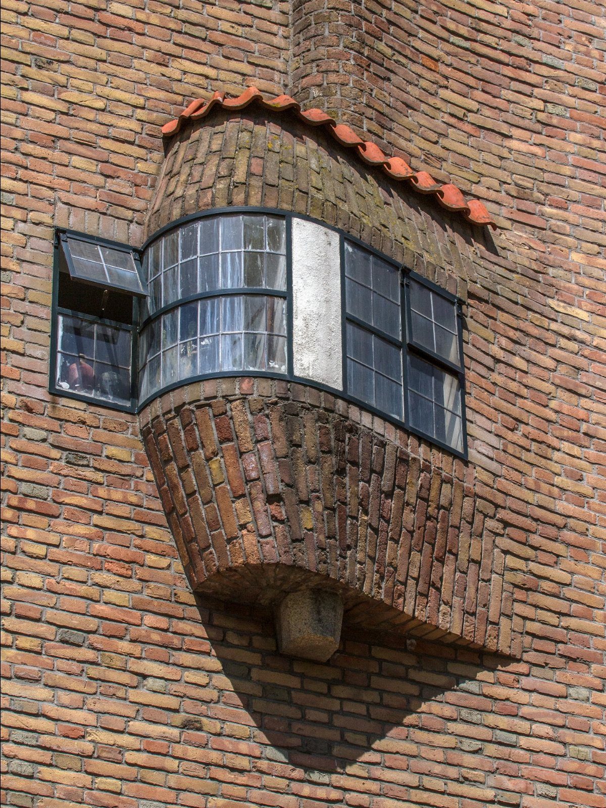 A curved brick bay window with dark metal frames set into a red brick wall.