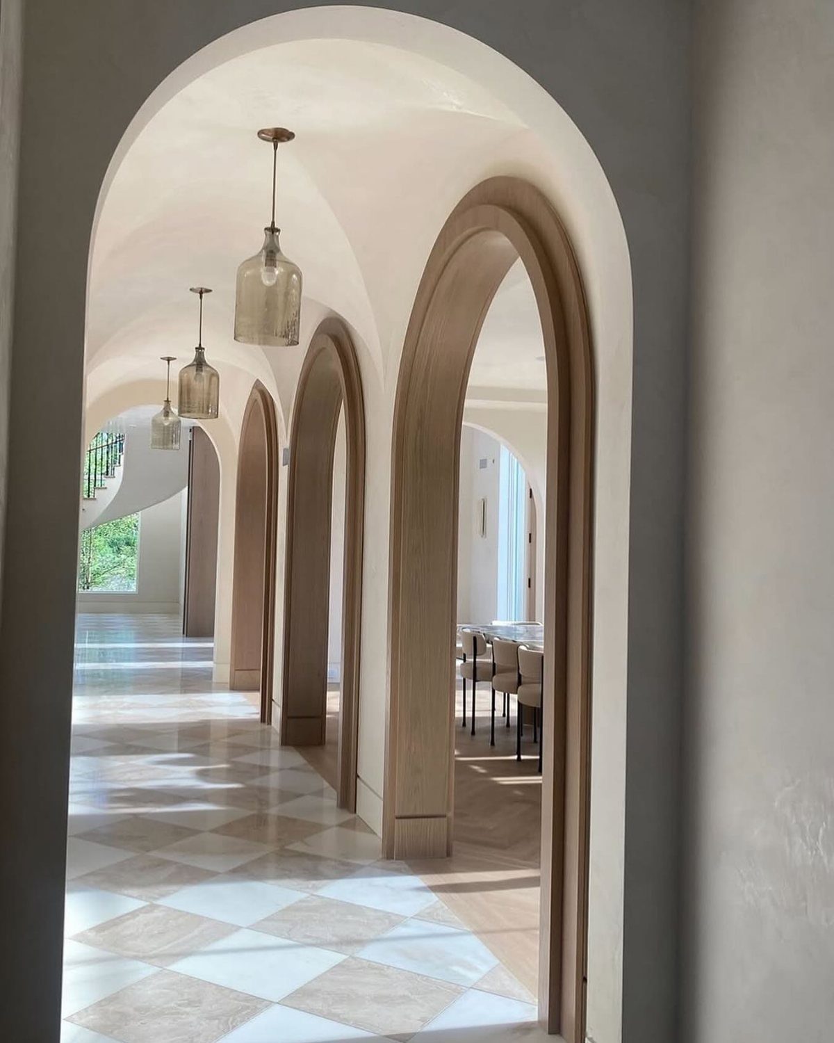 White arched doorways forming a hallway with checkered marble flooring and glass pendant lights.