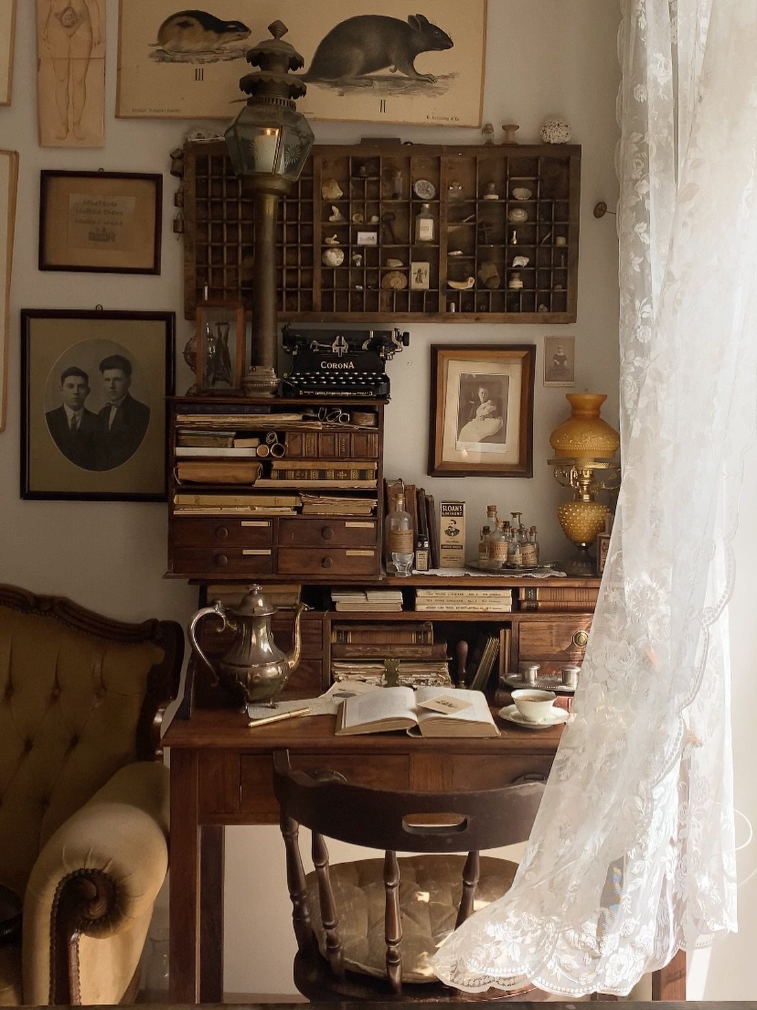 Vintage wooden desk featuring an antique typewriter, silver teapot, and framed old portraits.