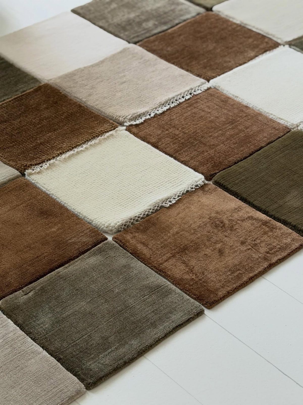 Patchwork rug with textured square tiles in earthy tones of brown, cream, and olive green.