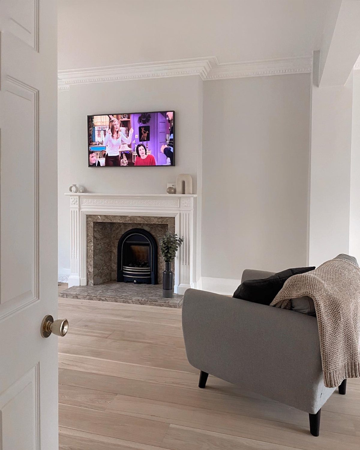 Bright living room with white walls, a white fireplace mantel, and a grey armchair.