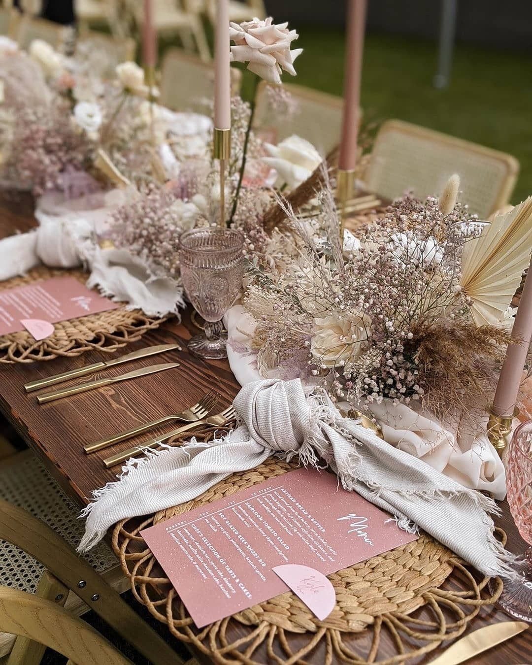 Dried wildflowers, pink roses, and taper candles arranged on a rustic wooden dining table.