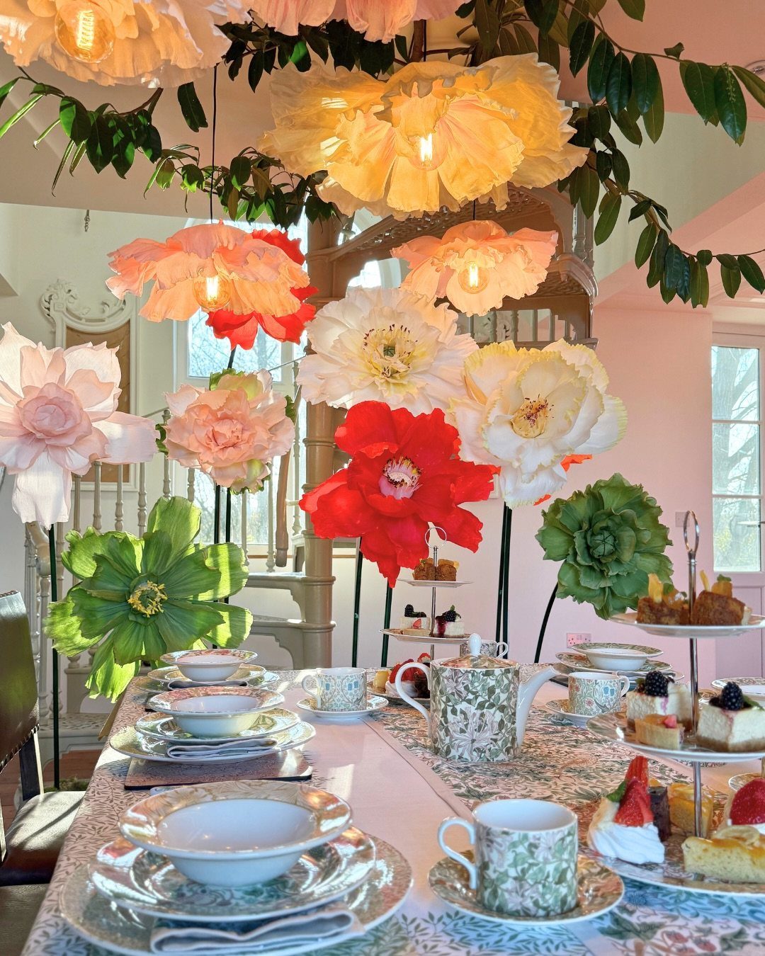 A decorated dining table with patterned tea sets under large, colorful paper flower decorations.