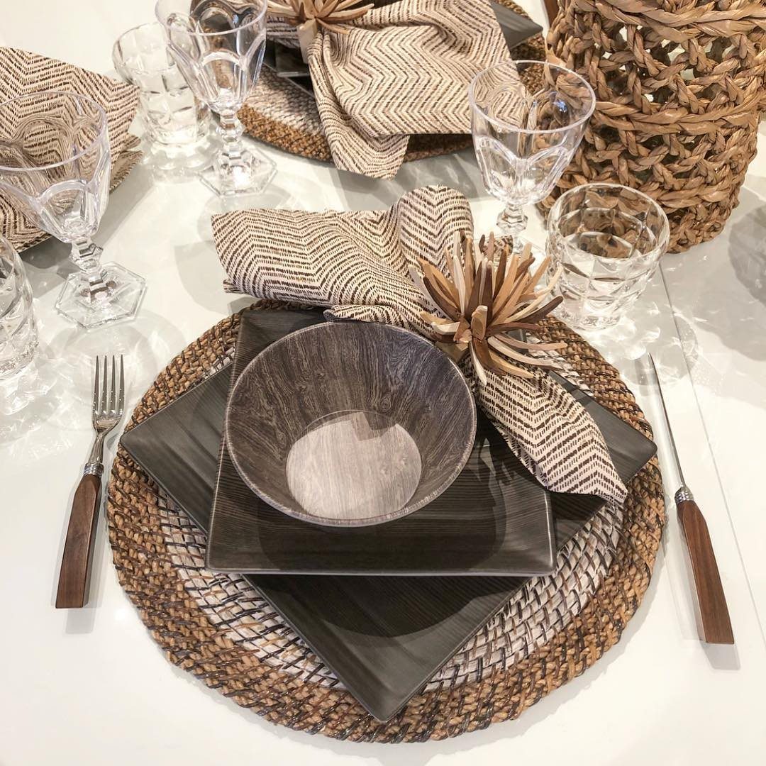 A modern table setting with dark square plates, woven placemats, and patterned napkins.
