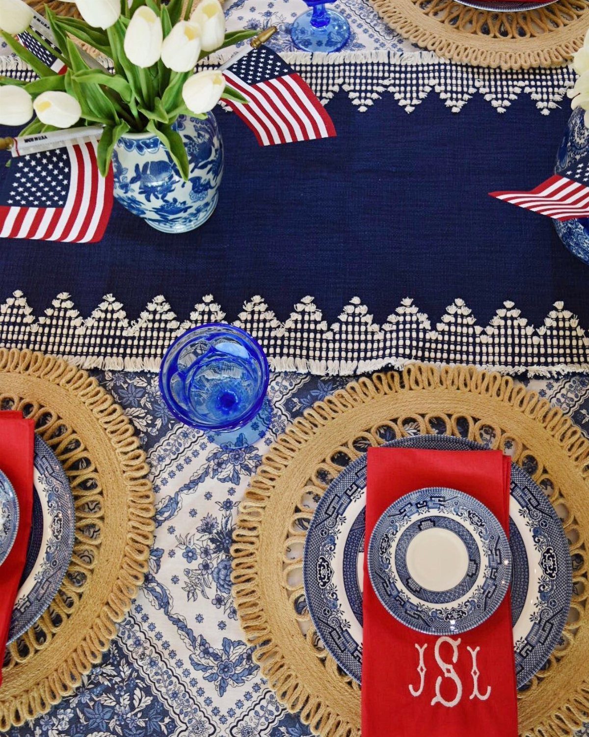 A patriotic summer tablescape with red napkins, blue patterned plates, and small American flags.