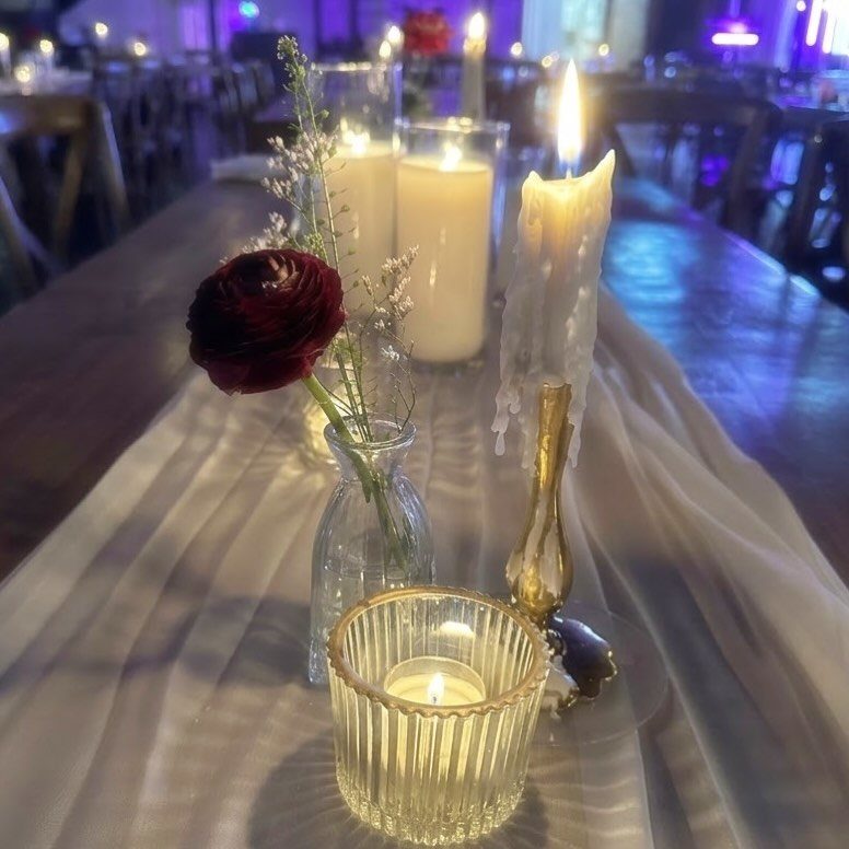 Lit candles and a single red rose on a long table with sheer white fabric.