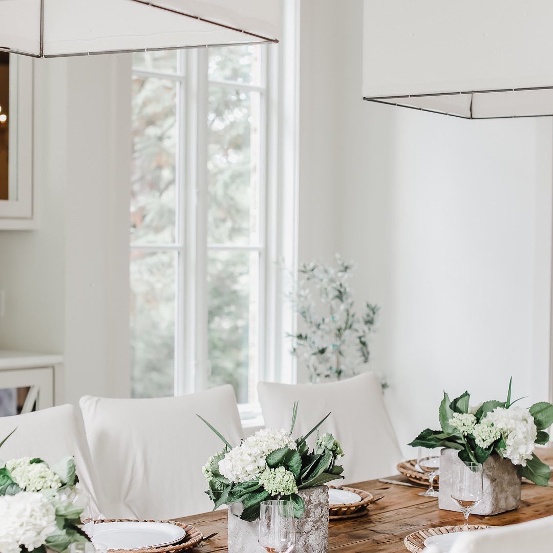 White hydrangeas in stone vases serve as simple centerpieces on a wooden dining table.