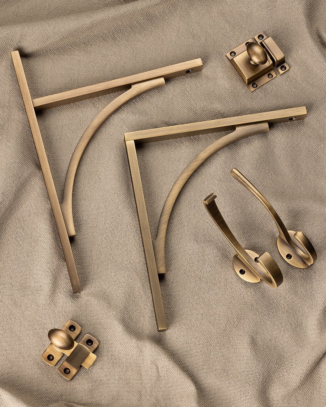 Antique brass hardware pieces including brackets and knobs resting on taupe textured fabric.